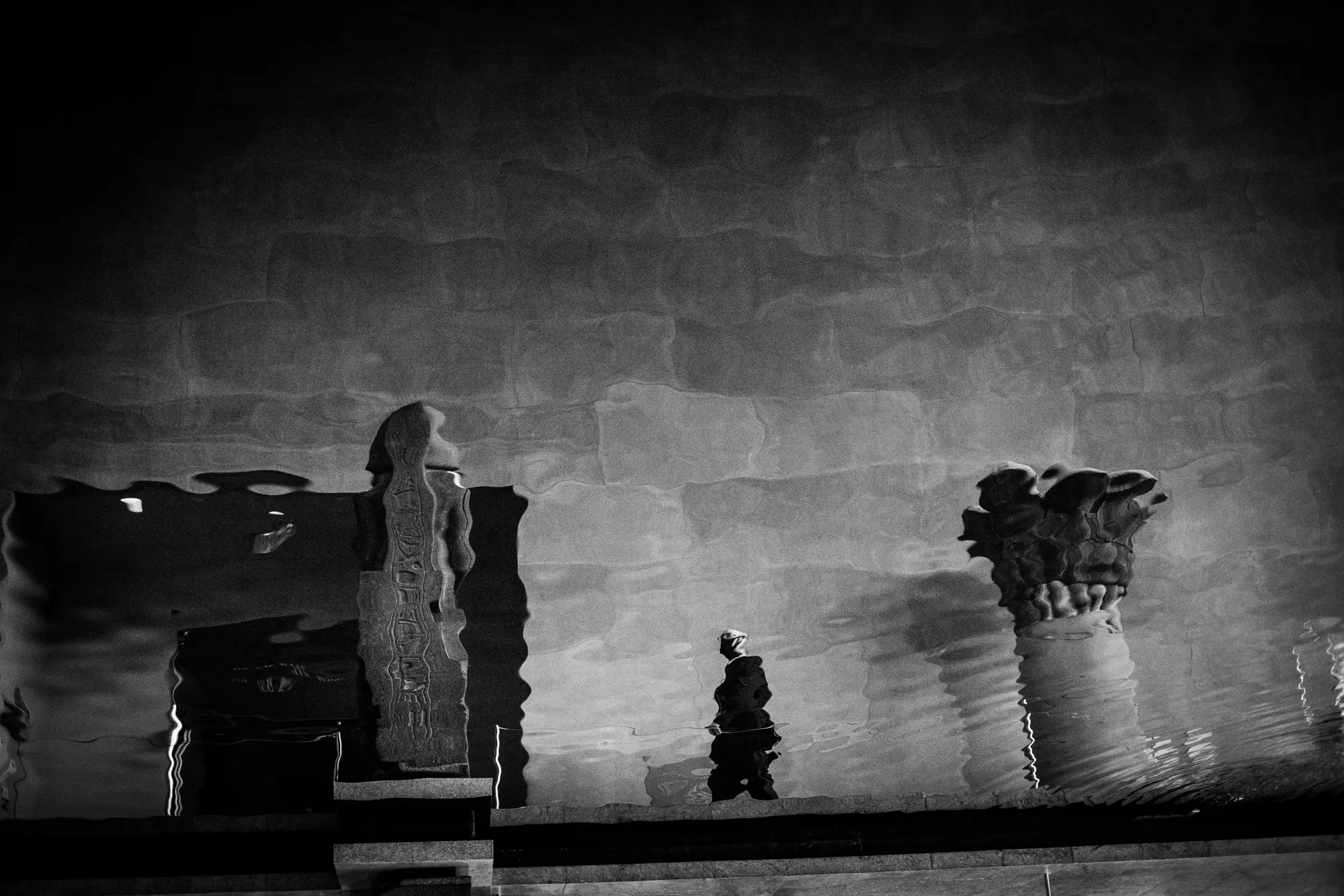 Figures and statues reflected across a dark wall